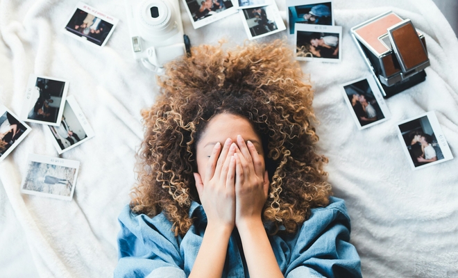 Woman surrounded by photo snapshots with eyes closed thinking of her memories